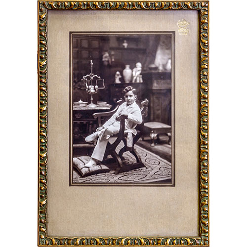Sub.:1-On - Lote: 641 -  Fotografa de un joven sentado sobre una jamuga. Enmarcada sobre fondo de terciopelo gris y con marco moldurado de estuco.