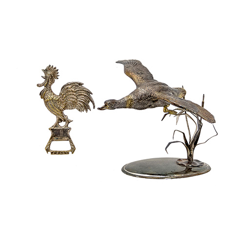 Sub.:10 - Lote: 1551 -  Centro de mesa en plata con pato en vuelo y abrebotellas en metal plateado con remate de gallo. Peso de la plata: 85 g.