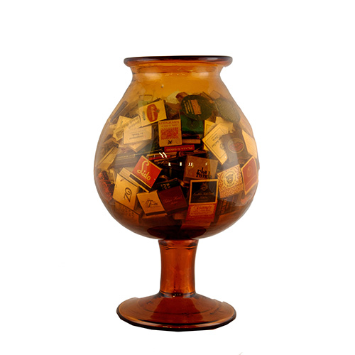 Sub.:10 - Lote: 500 -  Gran copa decorativa en cristal color mbar. Contiene una extensa coleccin de cerillas de diferentes procedencias.