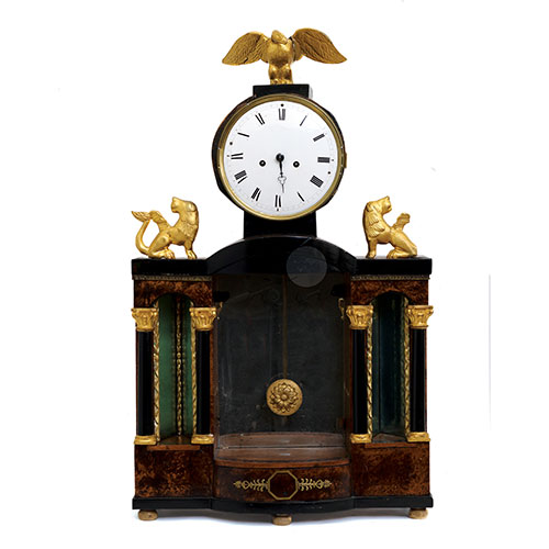 Sub.:23 - Lote: 317 -  Reloj de sobremesa en madera natural, dorada y ebonizada con cuatro columnas, dos figuras de len y remate de guila dorada. 