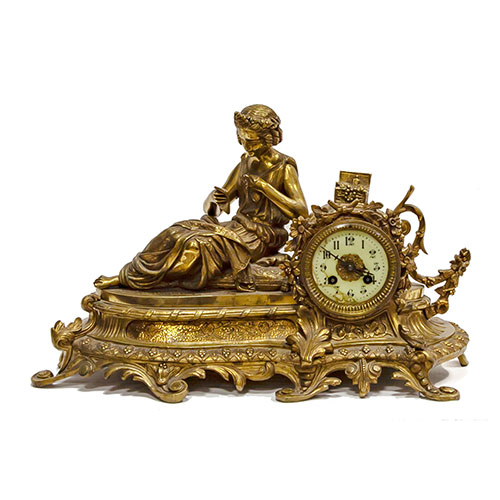 Sub.:24 - Lote: 1322 -  Reloj en bronce dorado con figura recostada leyendo, esfera en esmalte con numeraci�n ar�biga. 