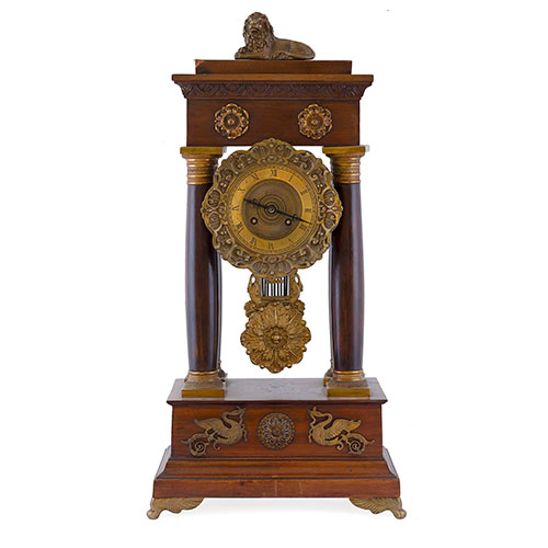 Sub.:27 - Lote: 1150 -  Reloj de sobremesa en madera de caoba con columnas. Apicaciones en bronce dorado y remate de len en reposo