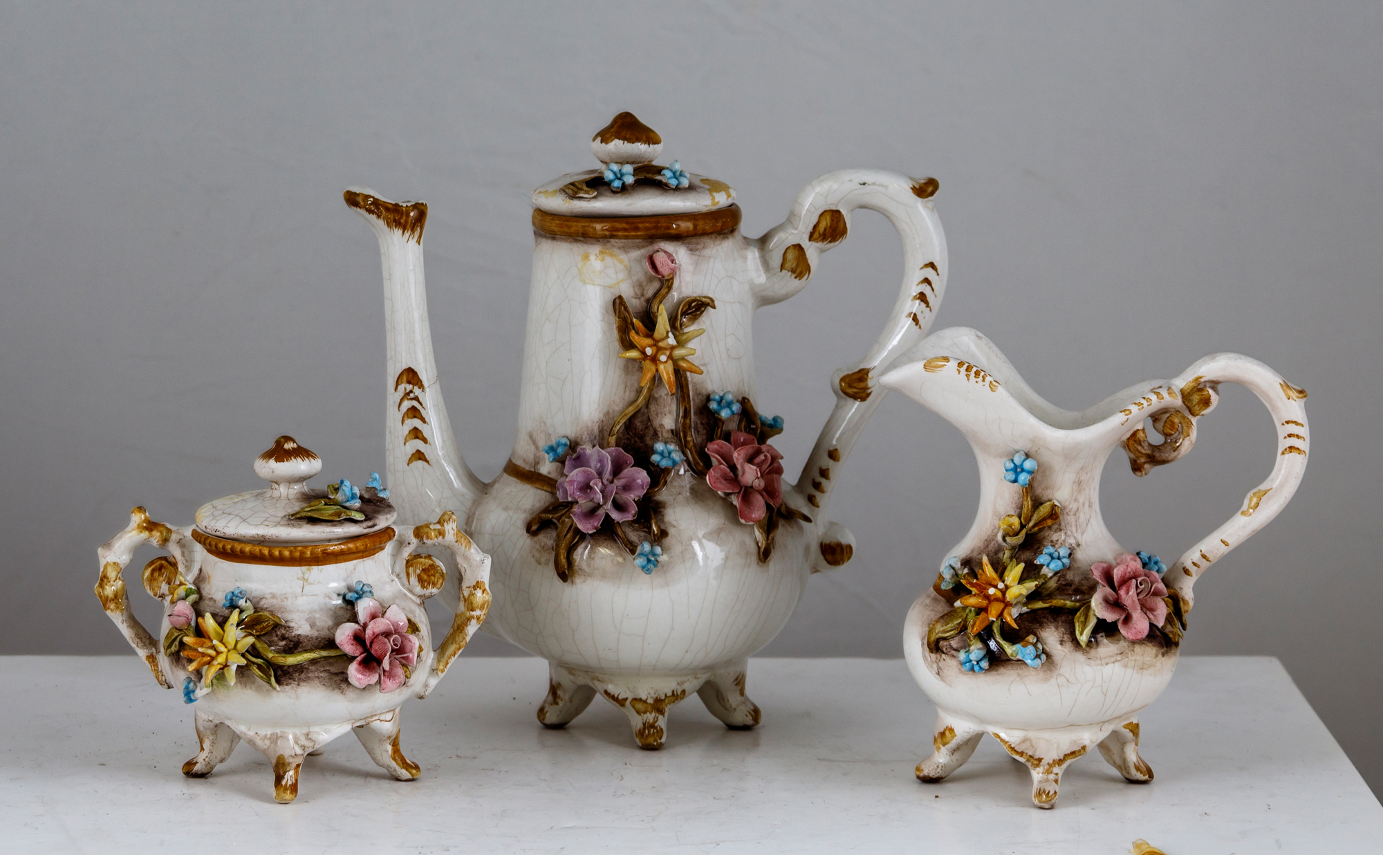 Sub.:3-On - Lote: 323 -  Lote formado por peque�a tetera en cer�mica vidridia con aplicaciones florares y vertedor roto, lechera y azucarero.