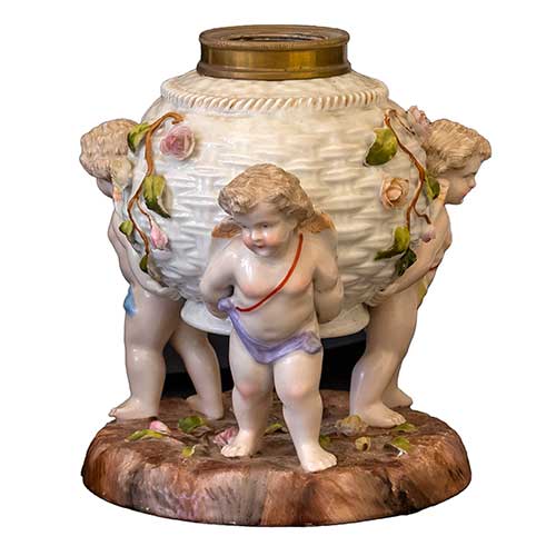 Sub.:34 - Lote: 239 -  Centro en porcelana con forma de canasto de mimbre sustentado por tres angelotes.