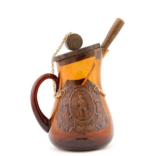 Sub.:6-On - Lote: 202 -  Jarra en vidrio con tapa de madera y cuchara para remover. Posee dos adornos de cuero en los laterales con figuras del Quijote.